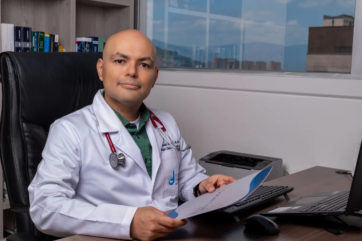 Dr. Daniel Amaya sosteniendo una carpeta clínica en su consultorio, con vista de Medellín de fondo